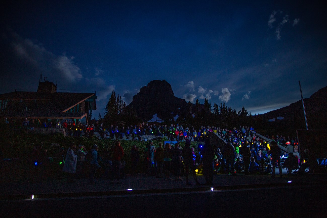Visitors gather to watch a short introduction under the night sky in front of a visitor center building.
