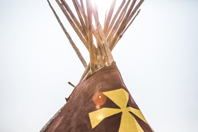 The top of a Blackfeet painted lodge is backlit by the sun.