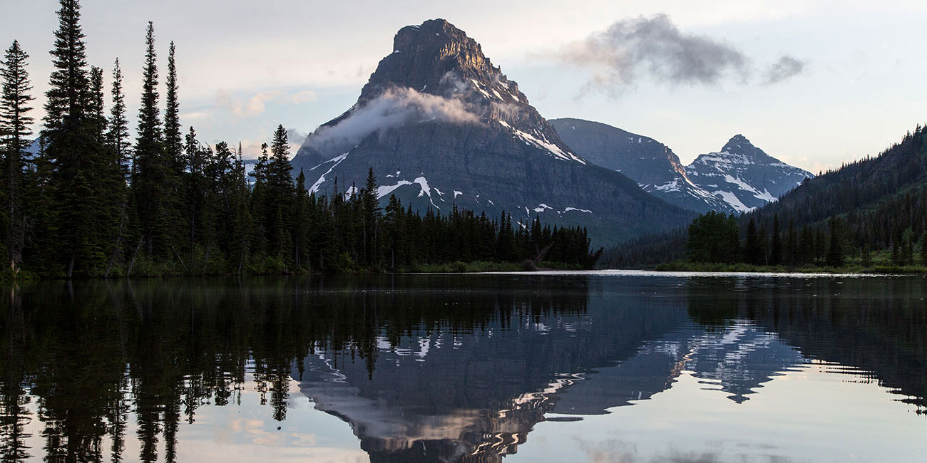 A tall mountain reflects in the waters of a calm lake during the early morning light.