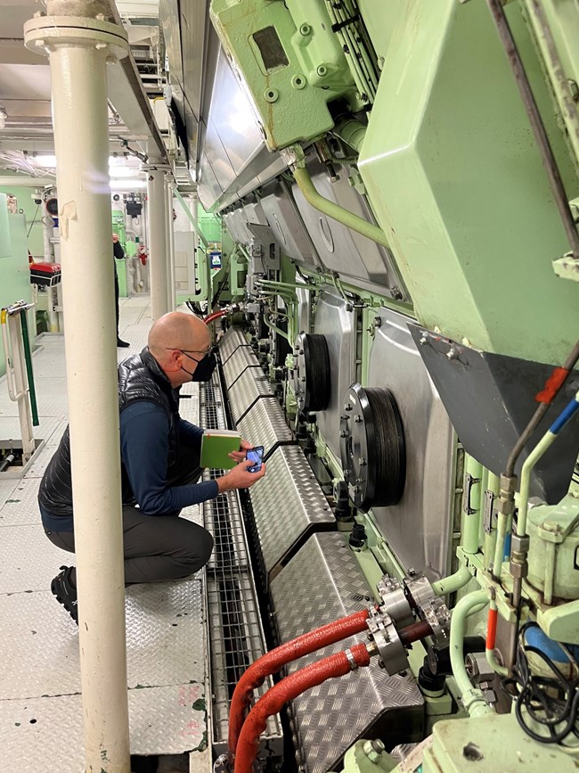 Inspector looking at cruise ship engine components in a brightly lit engine room.