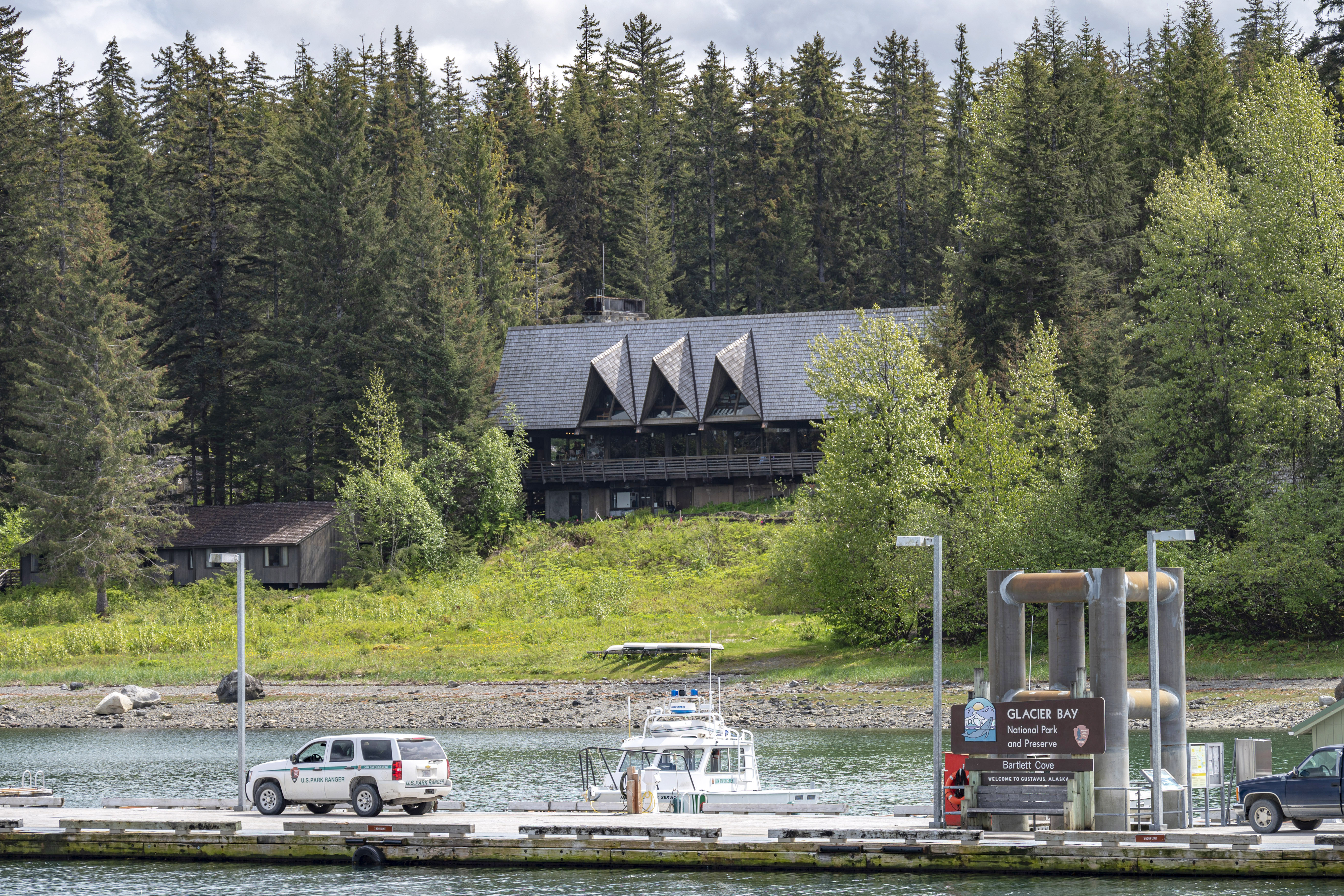 The Glacier Bay Lodge nestled in a dense forest on the shore of Bartlett Cove, the dock is visible in the foreground.