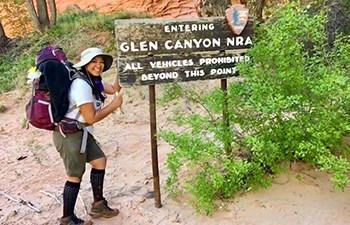 Young backpacker gives a thumbs up at wooden routered Glen Canyon entrance sign