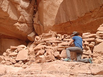 Park ranger kneels at base of sandstone and mortar ancient structure with repair tools
