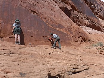 Two park rangers using scrub-brushes to clean etched-in graffiti from sandstone wall