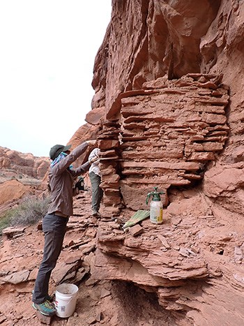 park ranger reaches to top of a sandstone and masonry ancient structure