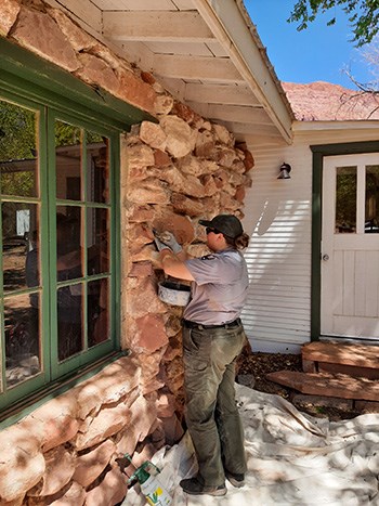 Park Ranger uses mortar tools on the outside wall of a stone house
