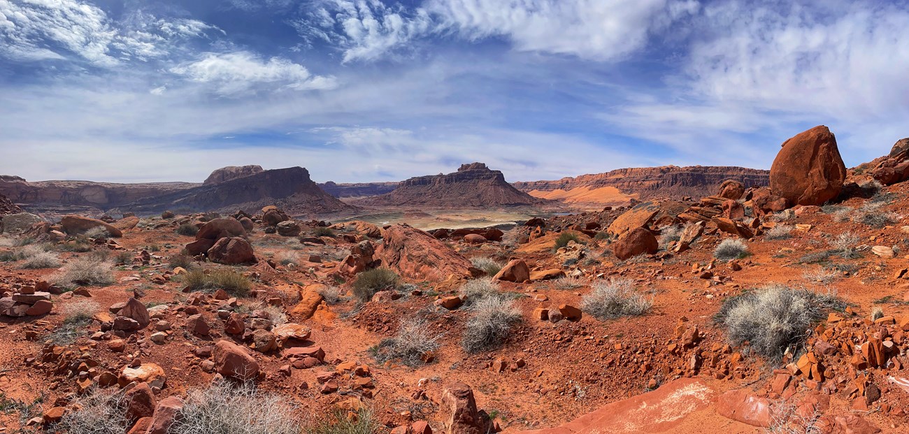 sweeping landscape with blue skies, jagged sandstone rocks, a desert lake, buttes, mesas, and a mountin.