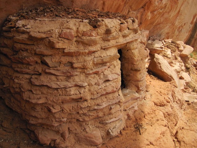 Nestled into a buff-colored canyon wall is an archeological site - a curved masonry structure that is structurally intact.