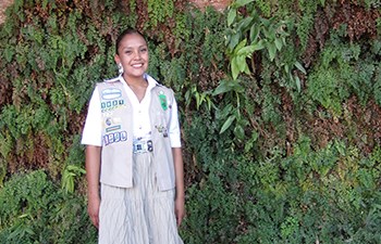 Girl Scout in uniform stands in front of a hanging garden