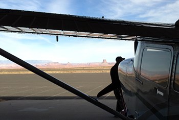 Man walks past plane in hangar with view of Tower Butte