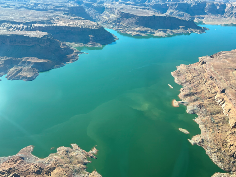 Aerial view of a desert lake in a sandstone canyon. The water at the lower half of the image is cloudy.