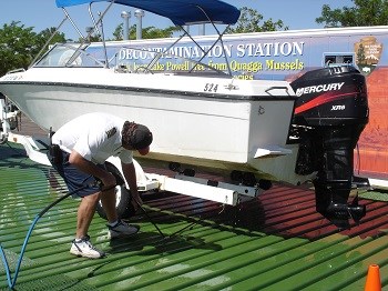 Man with power washer cleans underneath boat at park decontamination station