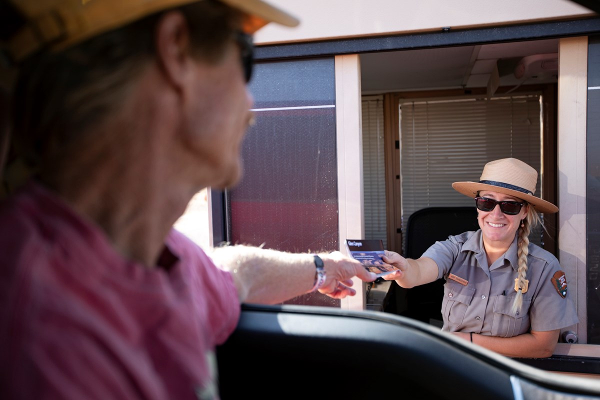 Ranger hands a brochure to a visitor behind the wheel of a car at at entrance booth