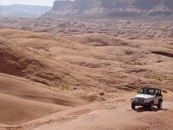 A jeep is dwarfed by surrounding red rock landscape