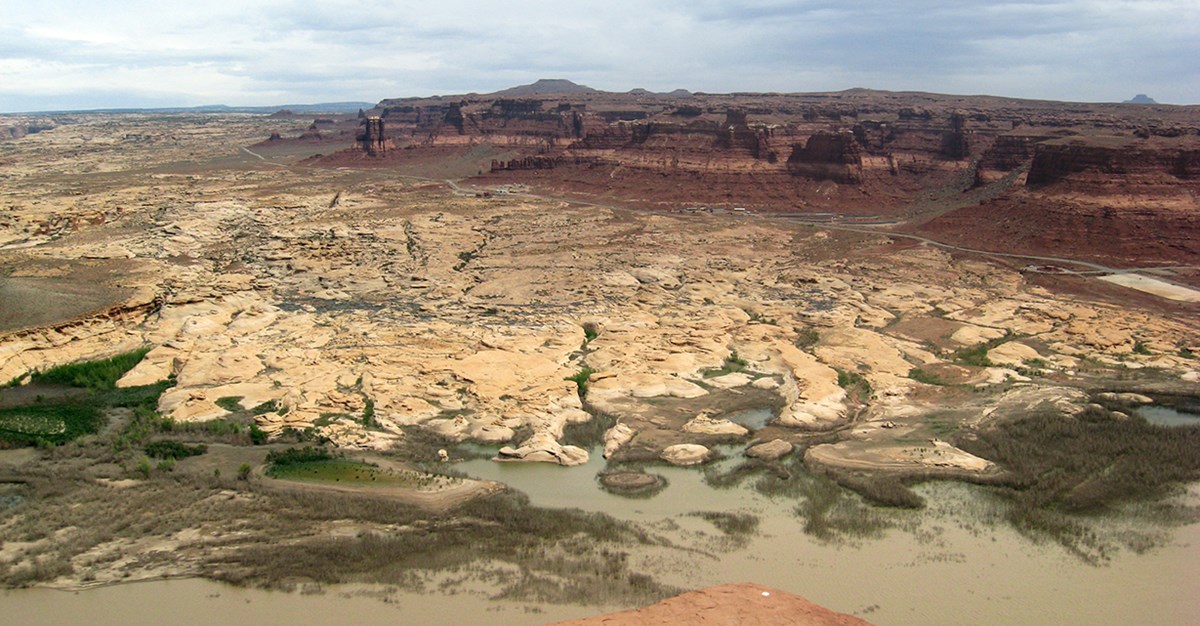Looking down from high overlook on red mesas giving way to rounded sandstone formations leading to waters edge