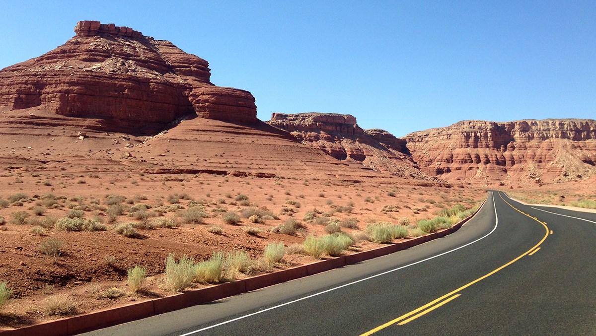 A paved road snakes by sandstone bluffs and cliffs