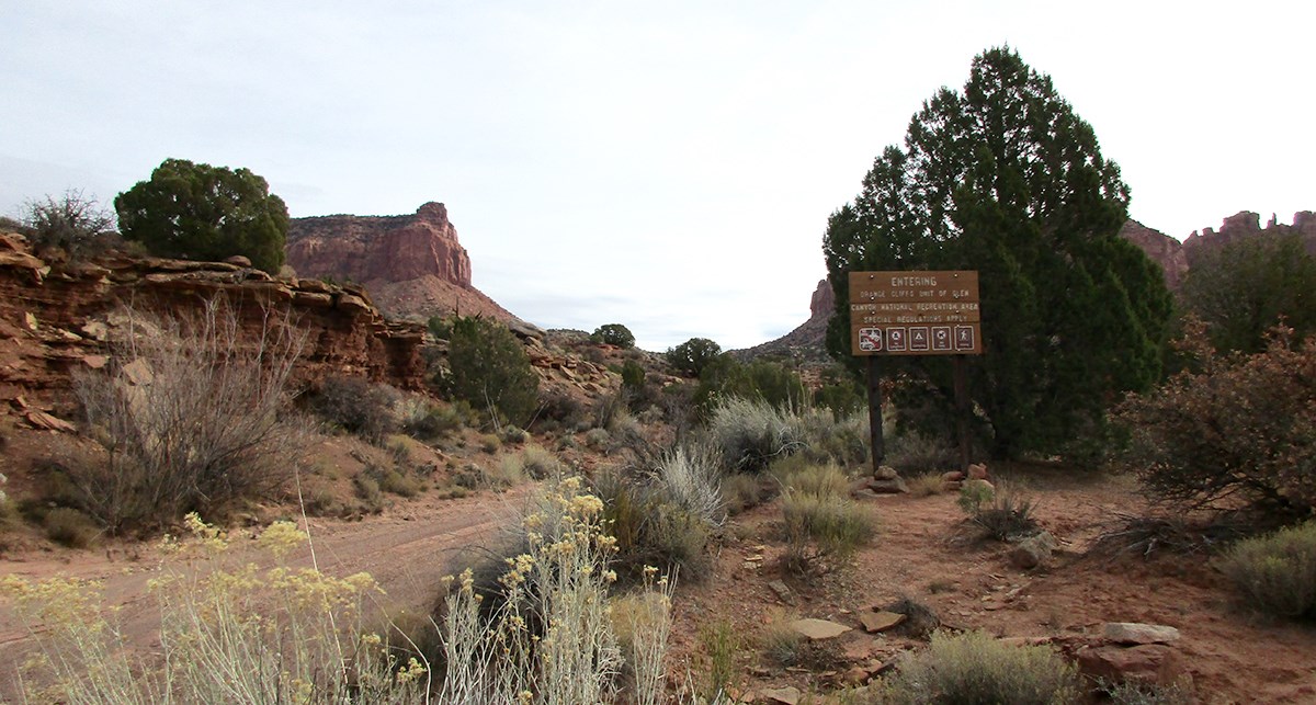 Dirt road among mesas leads past sign for Glen Canyon boundary