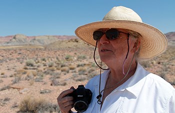 Woman wearing proper desert attire and holding camera looks over landscape