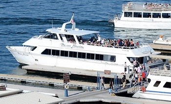 Group of people at marina loading onto a large boat with open roof deck