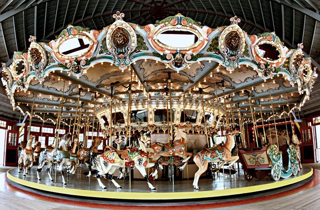 A carousel featuring a colorful menagerie of horses and other animals lit by a huge number of lights and mirrors.