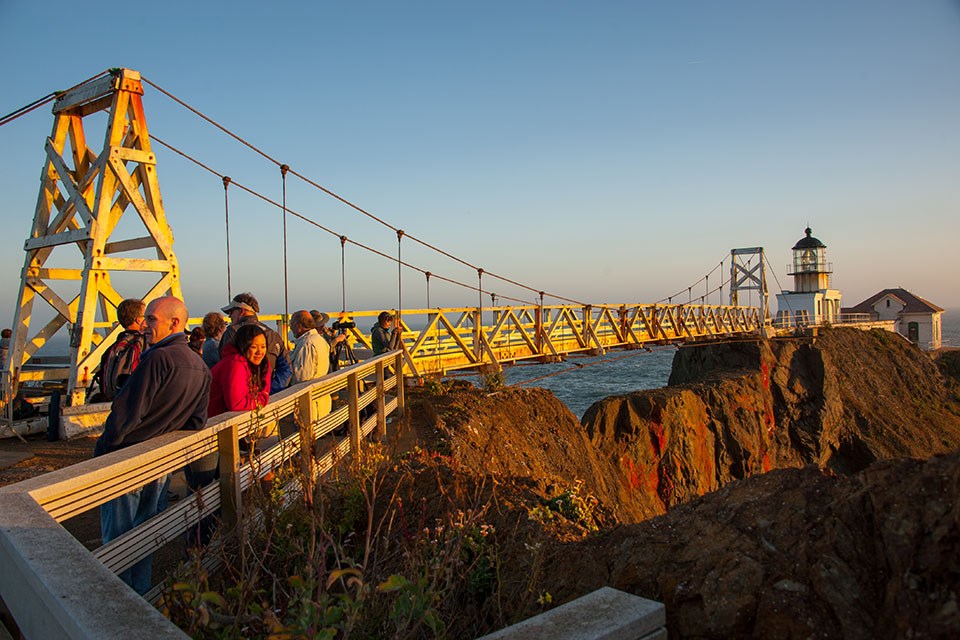 A small, white lighthouse building at the end of a suspension bridge