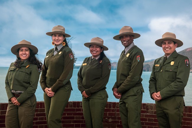 Five smiling rangers standing on the roof of Fort Point