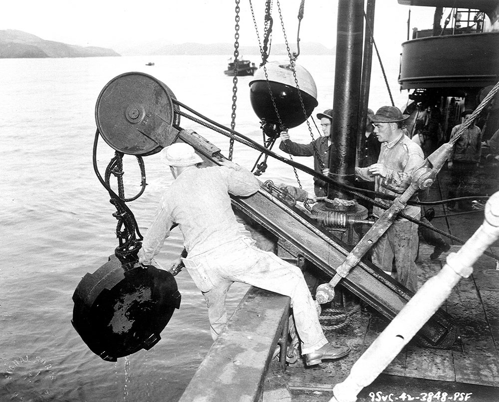 soldiers leaning over the side of a boat, pulling up large metal object