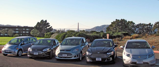 Five electric vehicles lined up at Fort Mason, with the Golden Gate Bridge in the background.