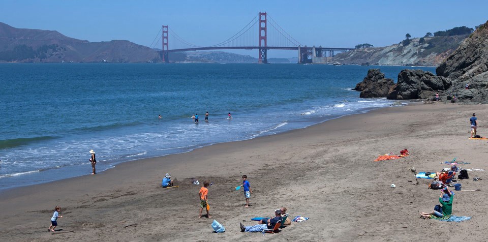 People playing and lounging on China Beach on a sunny day with Golden Gate Bridge behind