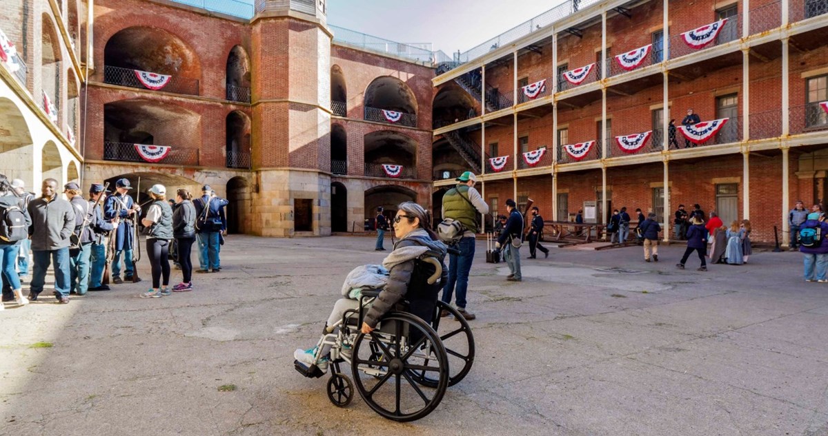 Person in wheelchair inside a brick fortress. Men dressed in civil war uniforms stand in the background.