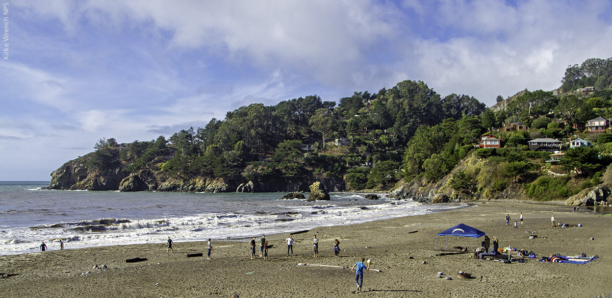 People playing on Muir Beach with the ocean and wooded hills in the background