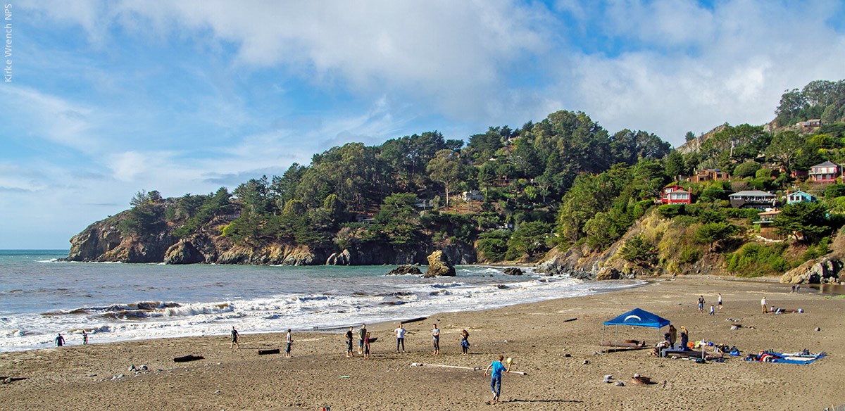 People playing on Muir Beach with the ocean and wooded hills in the background