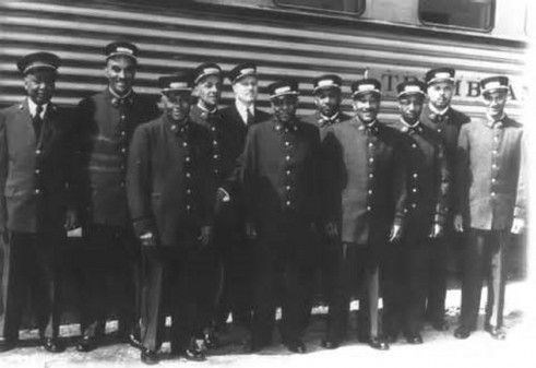 African American Pullman porters stand in front of a Pullman sleeping car.