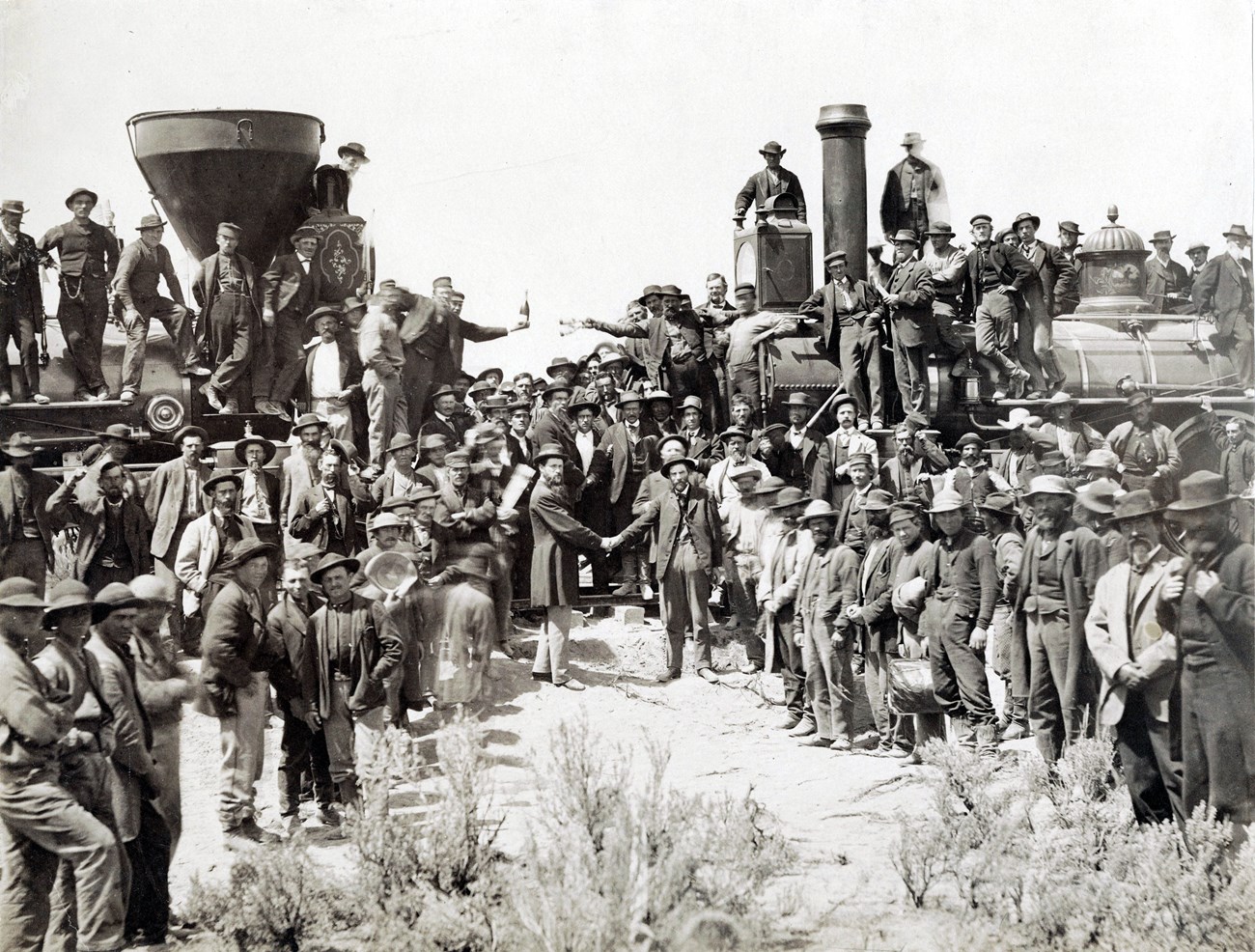 Men stand around two locomotives at the last spike site.