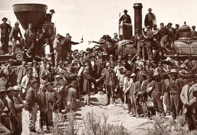 Men stand beside two locomotives celebrating the completion of the first transcontinental railroad.