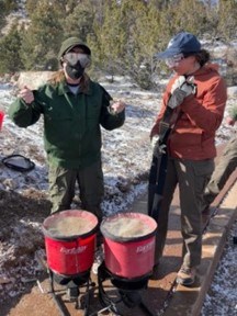 two people standing next to seeding buckets