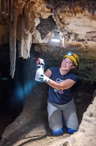 person spraying green algae next to cave light