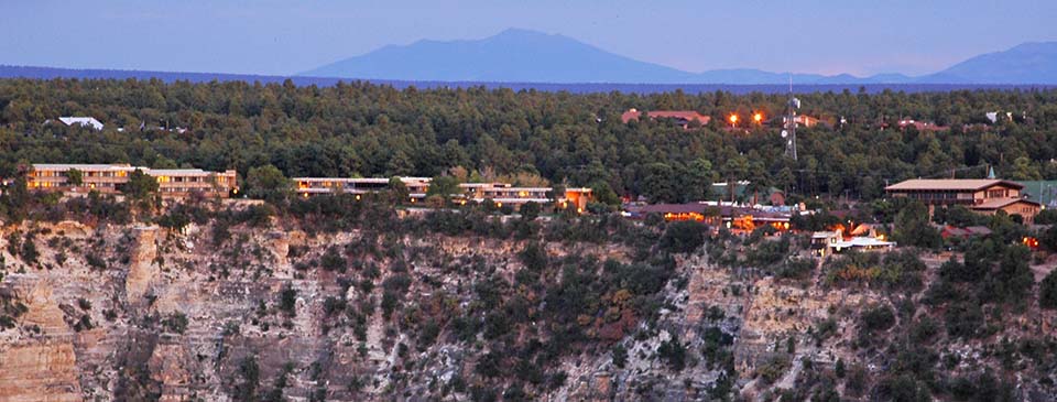 Overview of Grand Canyon Village as seen from a distance at twilight. Building lights are coming on.