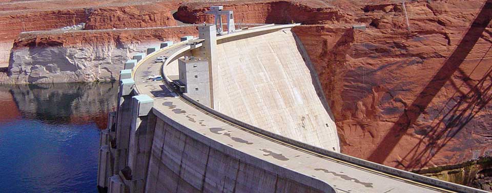 Side view of Glen Canyon Dam curving towards us. Lake water level is low.