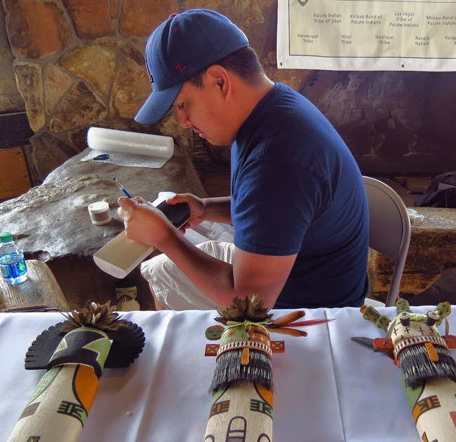 A man pains a wooden board with intricate and colorful designs that will later become a Hopi Kachina doll