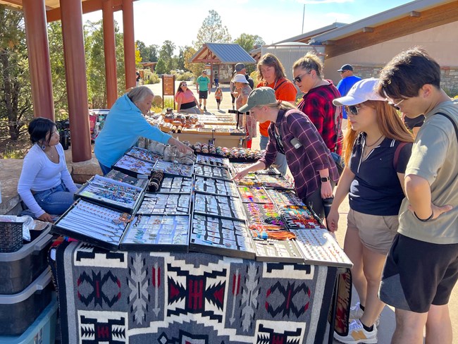 A table is adorned with native crafts while visitors stand next to a table looking at the crafts