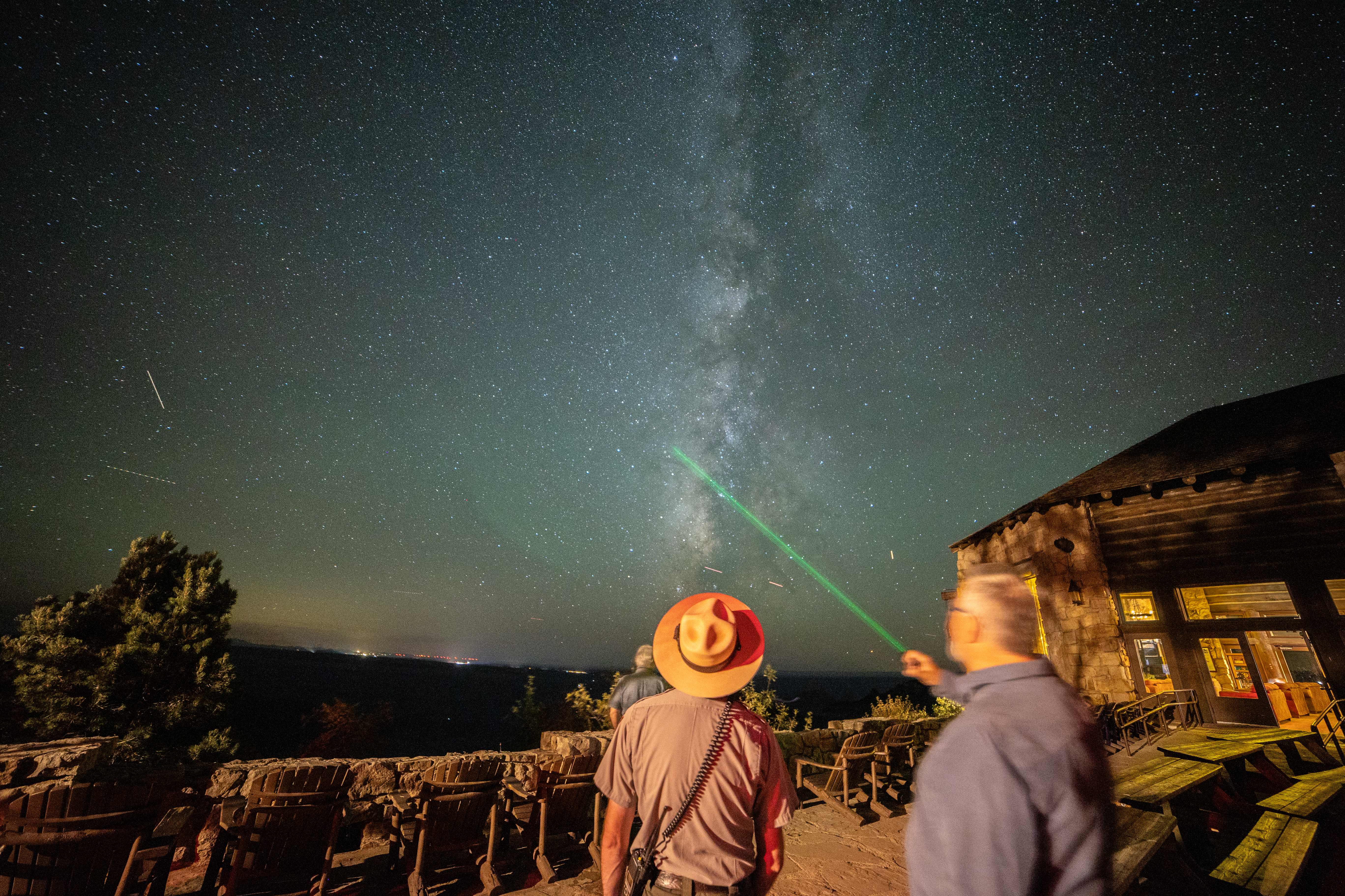 A ranger and a man stand under the stars as they point a green laser to the stars