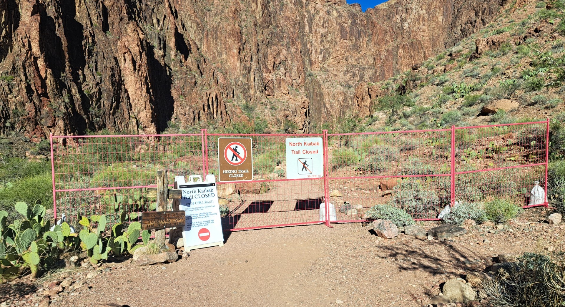 A red metal barricade with many signs stating the North Kaibab Trail is closed.