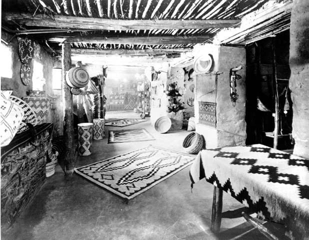 A black and white photo of a sales room with baskets and Navajo rugs.