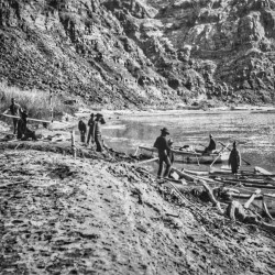 Men with boats on bank of river with cliffs in background