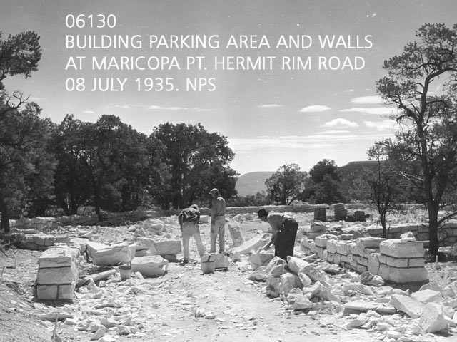Historic black and white photo of 3 CCC enrollees building a stone wall at a scenic overlook. chunks of rock and rubble are scattered about. Text: 06130 Building parking areas and walls, Hermit Rim Road, 1935.