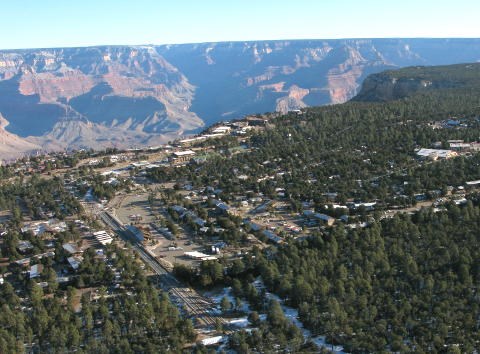 Aerial view of village roads, houses and buildings in a forested area on the edge vast canyon landscape of peaks and cliffs.