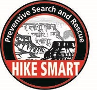 a black circle with a black line drawing of Grand Canyon inside. a banner across the front of the logo reads Hike Smart in white letters on a red background