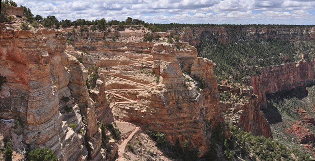 The rim of the canyon, showing light sandstone and switchbacks of a trail cutting through.