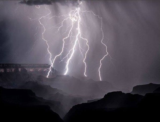 Multiple bolts of lightning illuminating the night and striking several nearby buttes within a canyon landscape of cliffs and peaks. Photo courtesy Daniel Pawlak